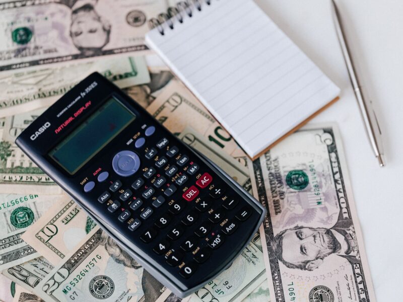 Calculator on dollar bills with a blank notepad nearby.