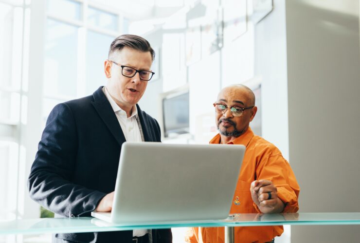 Two businessmen discussing work on a laptop in a modern office.
