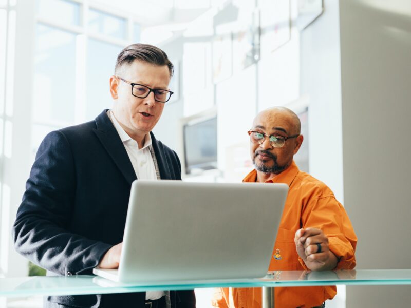 Two businessmen discussing work on a laptop in a modern office.