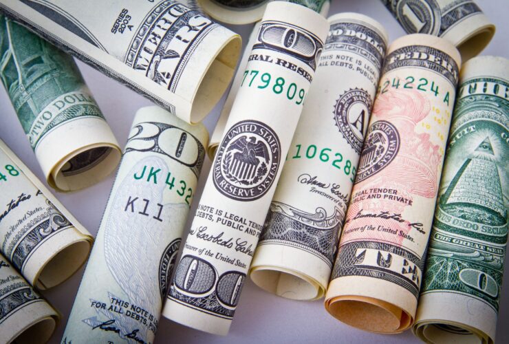 Rolled US dollar bills and a pen on a white surface.