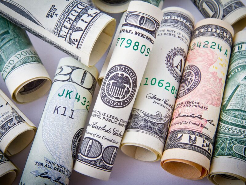 Rolled US dollar bills and a pen on a white surface.