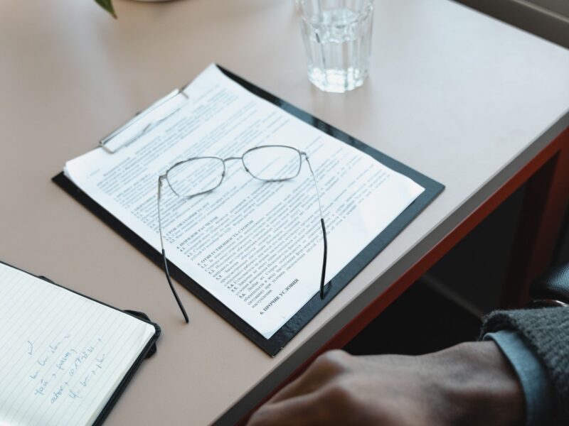 Person reviewing documents with eyeglasses on a table beside a glass of water.