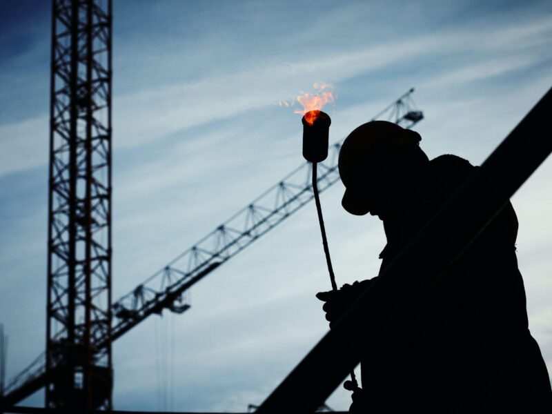 Silhouette of a construction worker with a crane and torch flame in the background.